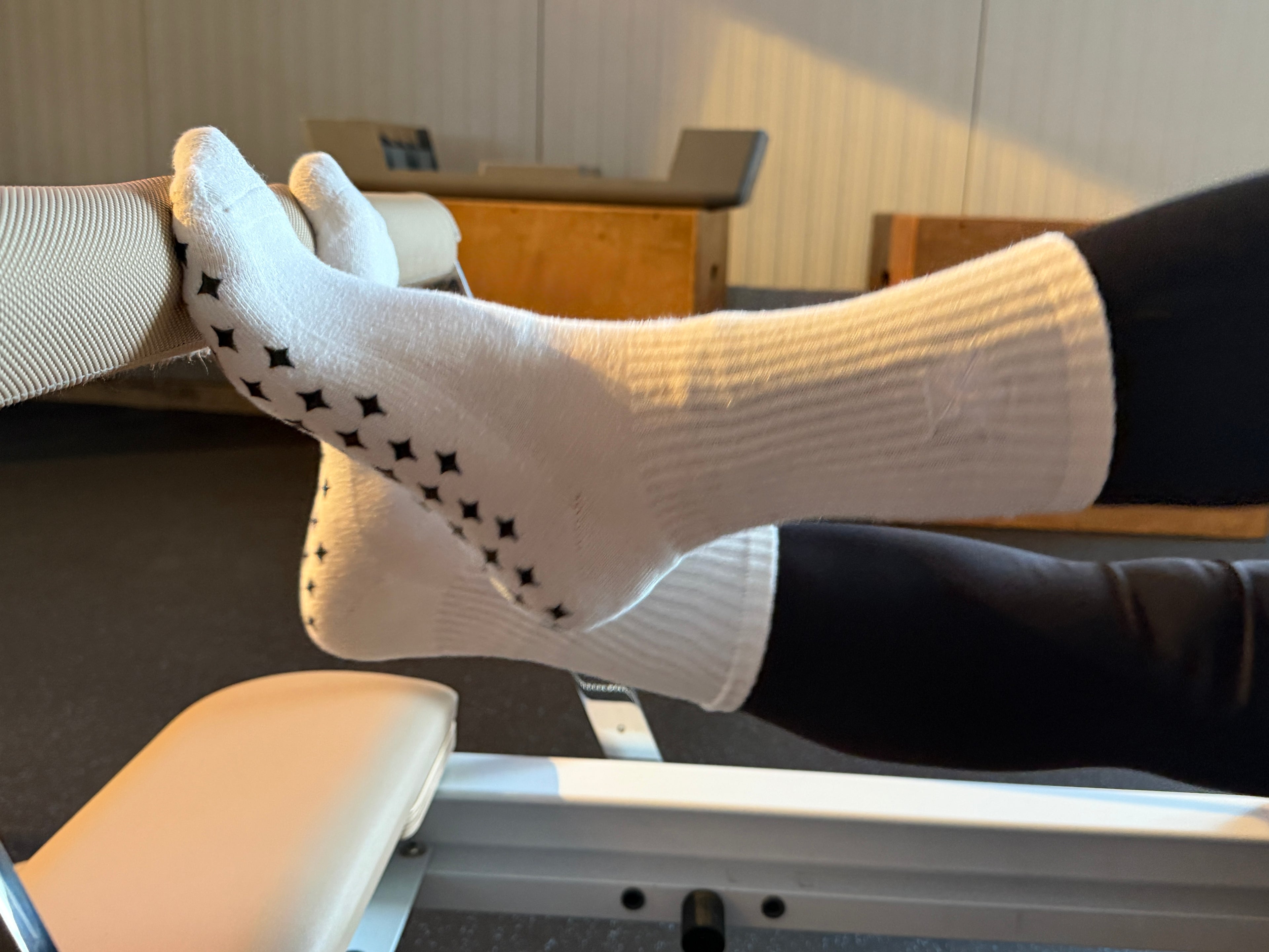 A person wearing white Yoga Stars grip socks with black star patterns while exercising on a reformer.